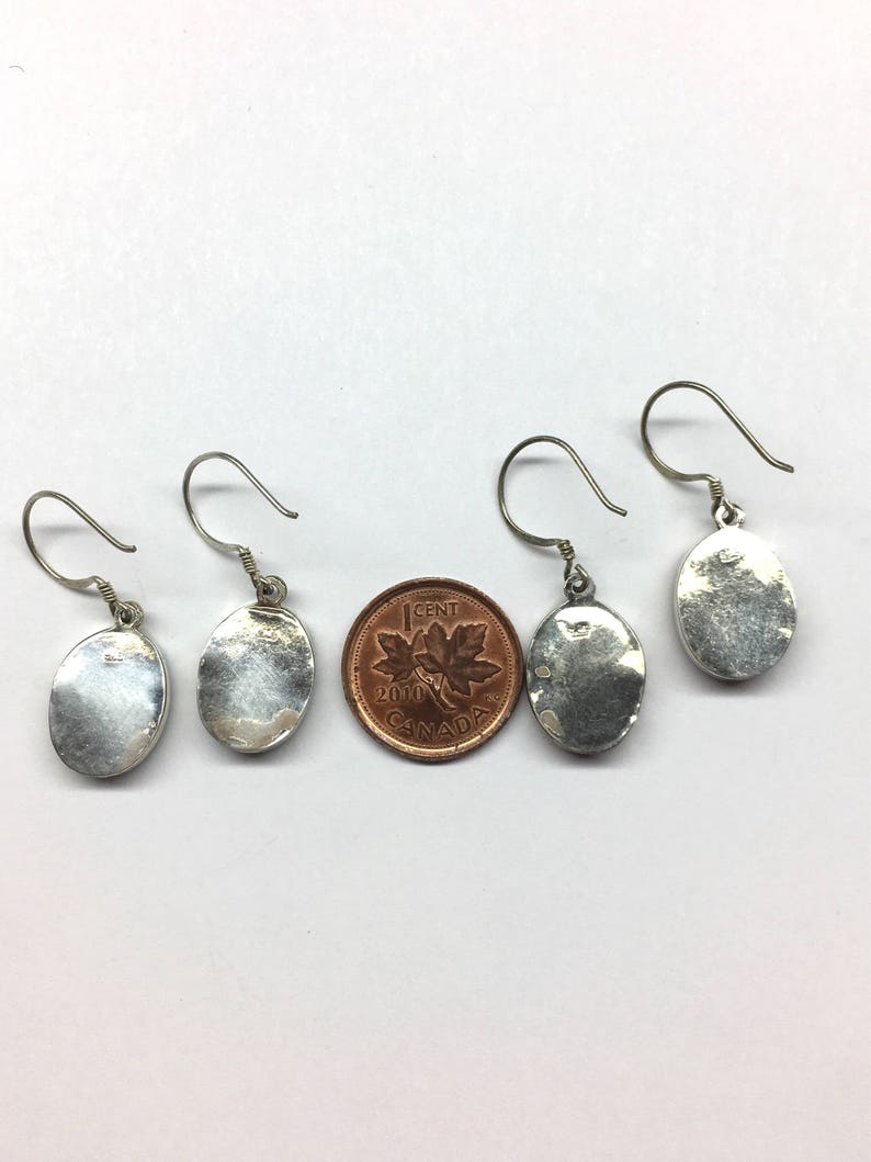 May include: Three pairs of silver oval earrings with a hook closure. The earrings are about the size of a Canadian penny.
