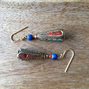 May include: A pair of dangle earrings with a gold tone metal setting. The earrings feature a blue and red stone with a turquoise accent.
