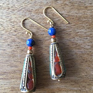 May include: A pair of gold dangle earrings with blue and red beads. The earrings feature a cone-shaped pendant with a turquoise and red stone design.