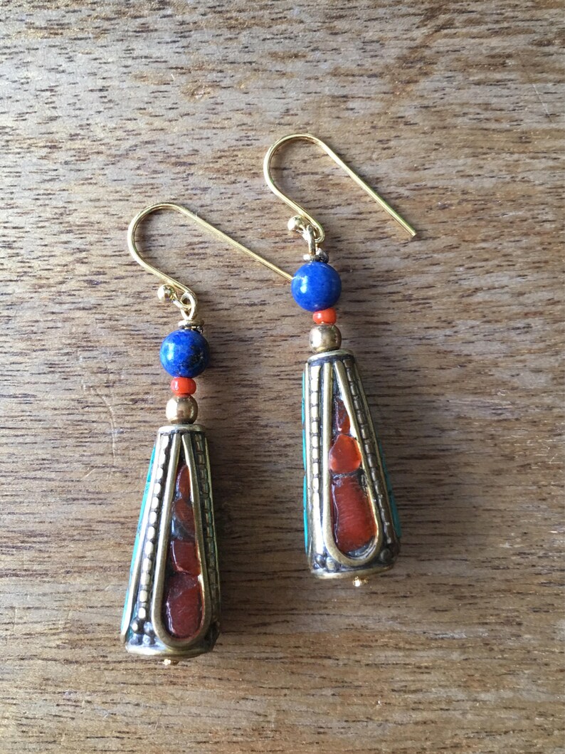 May include: A pair of gold dangle earrings with blue and red beads. The earrings feature a cone-shaped pendant with a turquoise and red stone design.