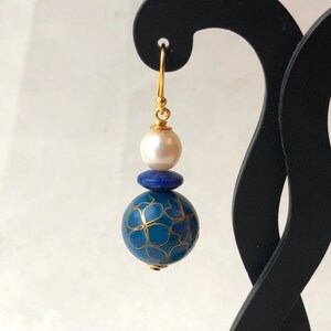 May include: Gold dangle earrings with a blue and gold patterned sphere, a small blue bead, and a white pearl.