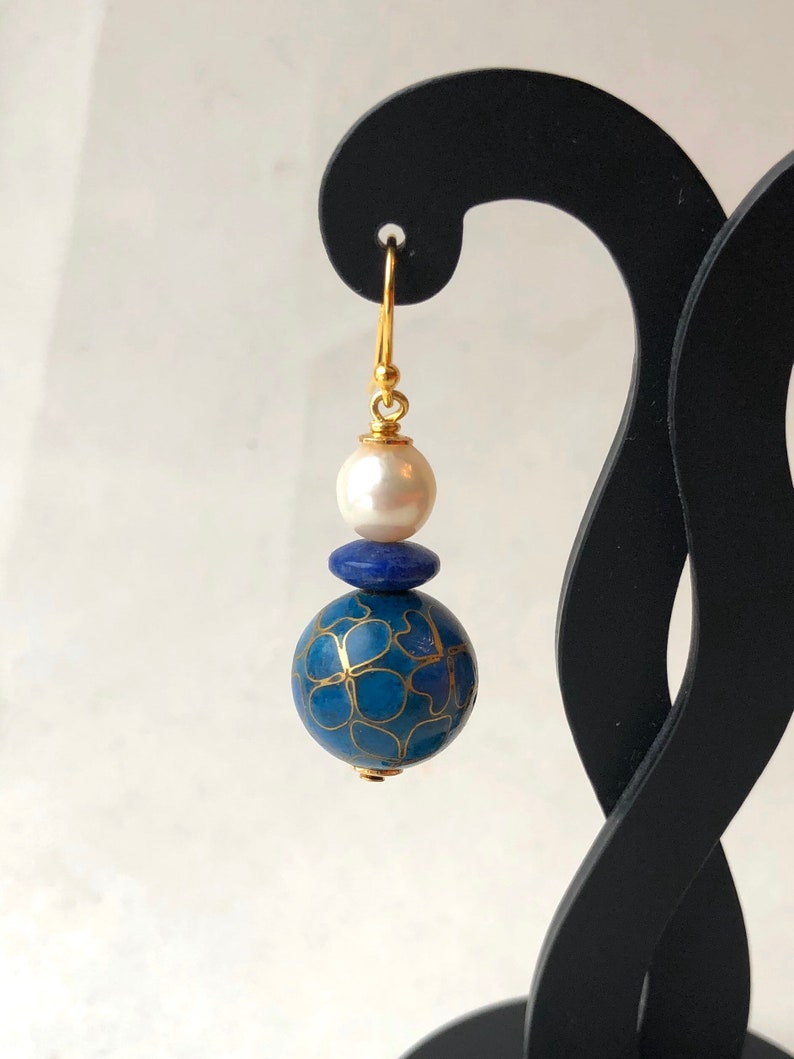 May include: Gold dangle earrings with a blue and gold patterned sphere, a small blue bead, and a white pearl.