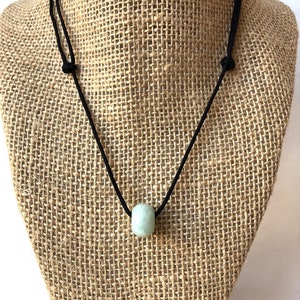 May include: A simple necklace with a single light green jade bead on a black cord.