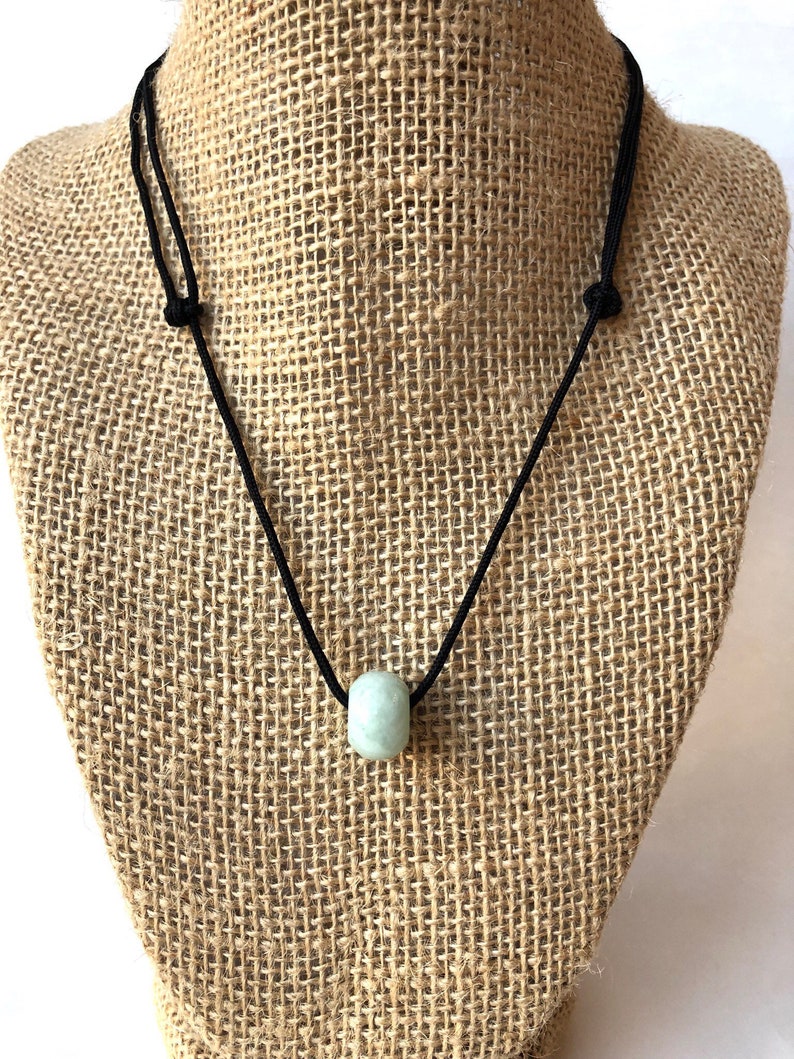 May include: A simple necklace with a single light green jade bead on a black cord.