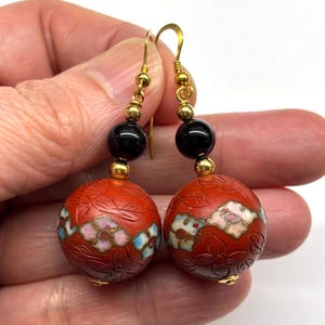 May include: Red and gold dangle earrings with black beads and floral designs.