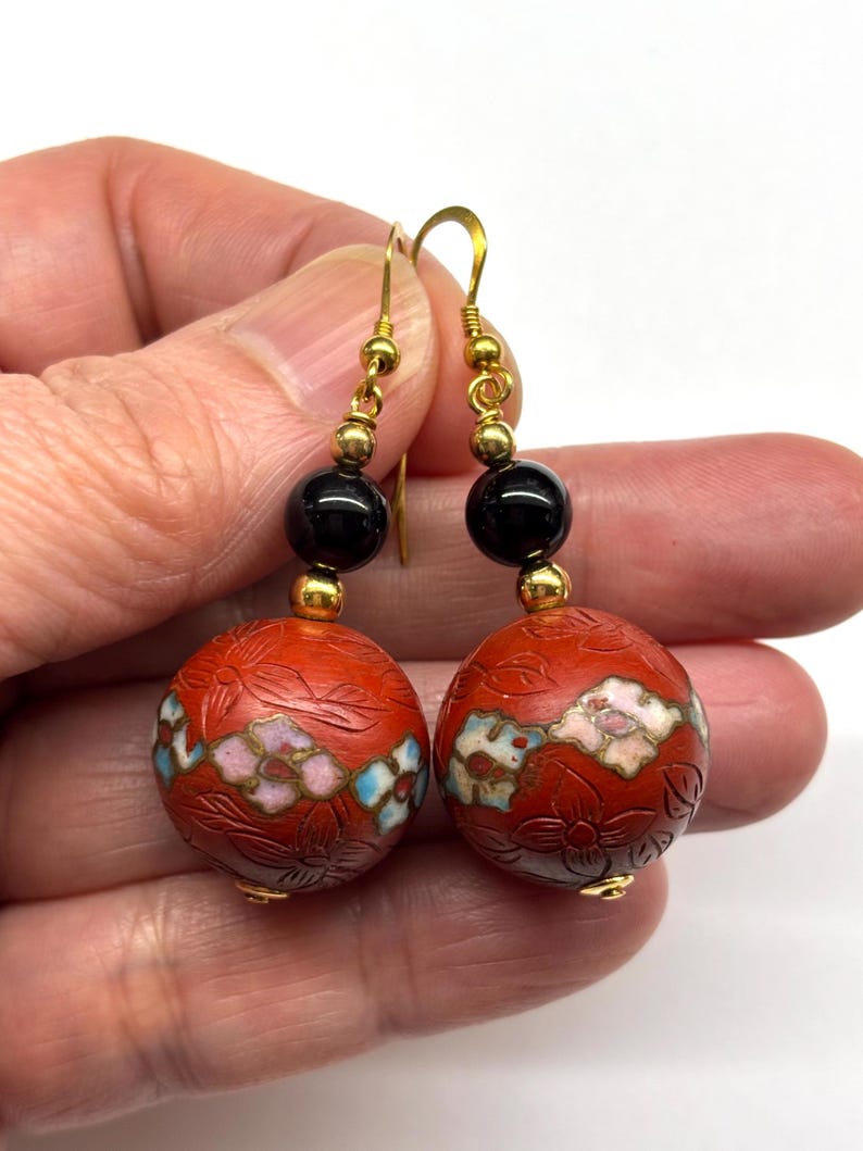 May include: Red and gold dangle earrings with black beads and floral designs.
