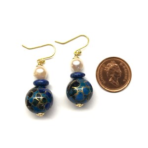 May include: A pair of gold earrings with blue and black enamel beads, white pearls, and gold accents. The earrings are approximately the size of a Canadian penny.