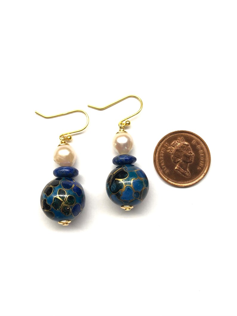 May include: A pair of gold earrings with blue and black enamel beads, white pearls, and gold accents. The earrings are approximately the size of a Canadian penny.