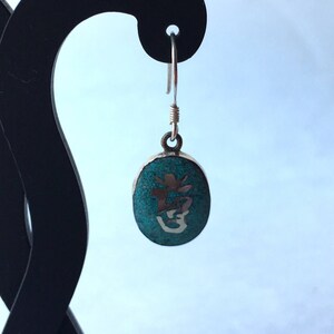 May include: Silver dangle earrings with a turquoise oval pendant featuring a silver Chinese character.