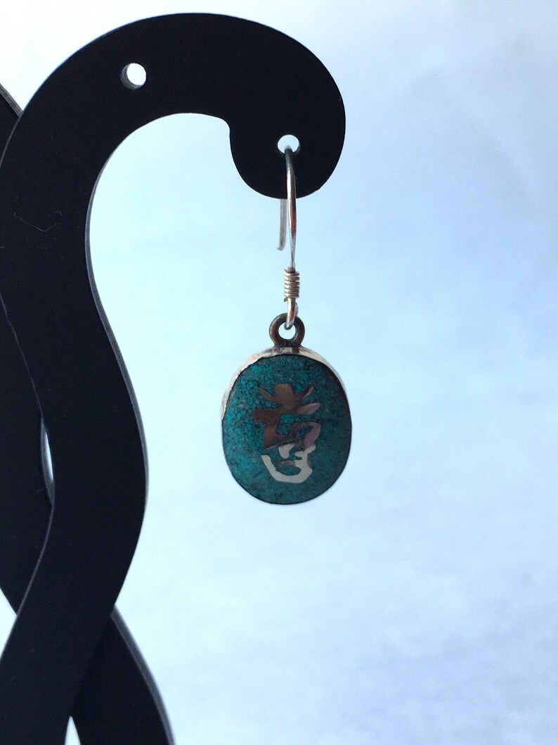 May include: Silver dangle earrings with a turquoise oval pendant featuring a silver Chinese character.