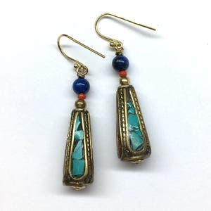 May include: A pair of gold dangle earrings with turquoise and red beads. The earrings have a teardrop shape and are accented with gold.