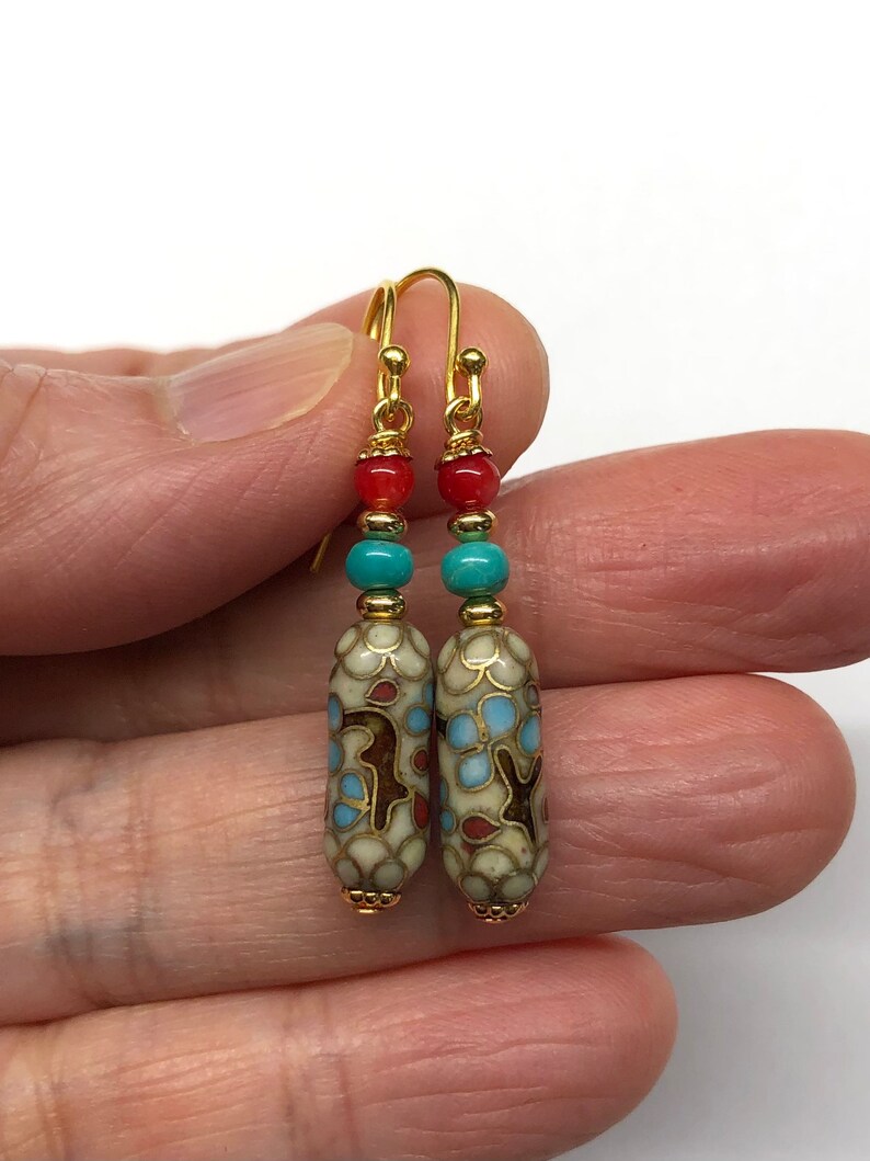 May include: Gold dangle earrings with a white, blue, and red patterned ceramic bead, a turquoise bead, and a red bead.