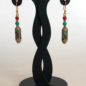 May include: A pair of gold dangle earrings with a white, brown, and blue patterned ceramic bead, a turquoise bead, and a red bead on each earring.