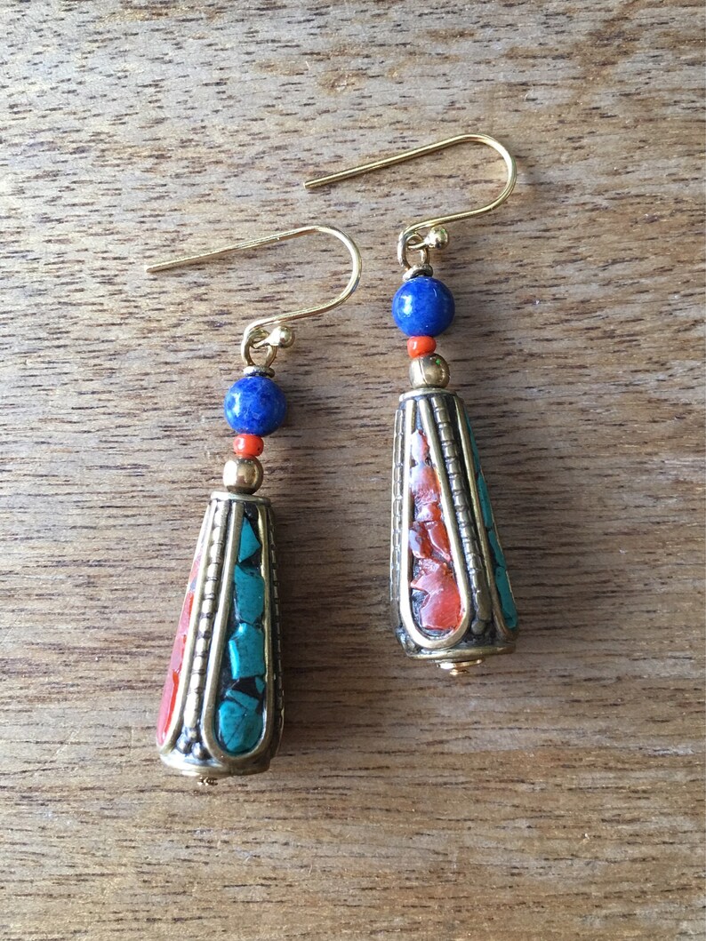 May include: A pair of dangle earrings with a gold tone finish. The earrings feature a teardrop-shaped pendant with a mix of turquoise, red, and orange stones. Each earring is topped with a blue lapis lazuli bead.