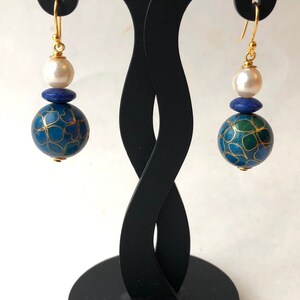 May include: A pair of gold earrings with a blue and green patterned sphere, a blue stone, and a white pearl on each earring.