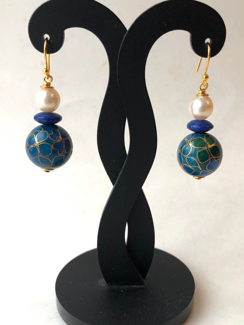 May include: A pair of gold earrings with a blue and green patterned sphere, a blue stone, and a white pearl on each earring.