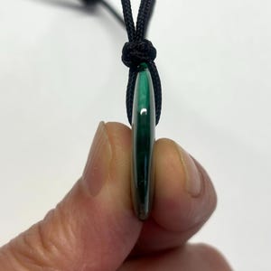 May include: A green malachite stone pendant on a black cord necklace.
