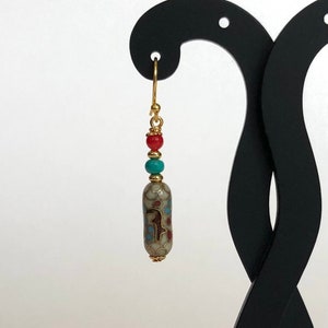 May include: Gold dangle earrings with a turquoise and red bead, and a white ceramic bead with a gold and blue pattern.