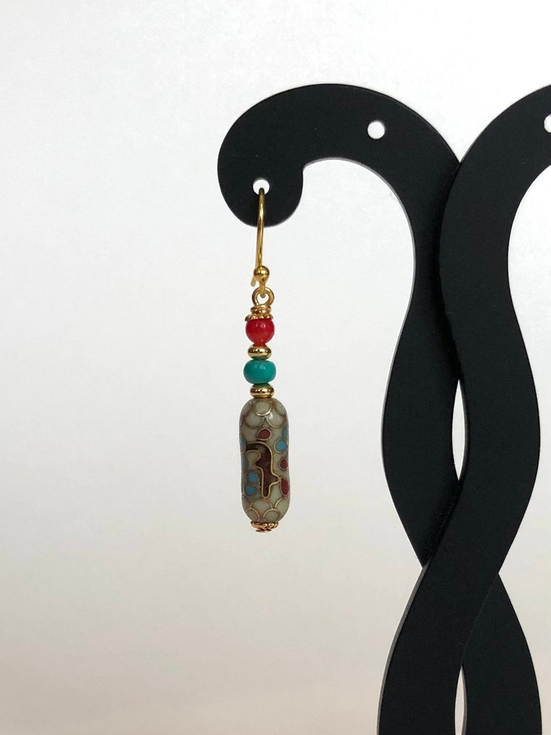 May include: Gold dangle earrings with a turquoise and red bead, and a white ceramic bead with a gold and blue pattern.