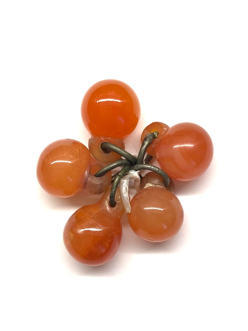 May include: A cluster of six orange carnelian beads connected by silver wire. The beads are teardrop shaped and have a smooth, polished finish.
