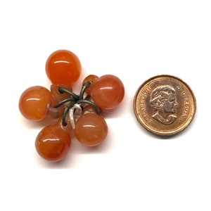 May include: A cluster of six small, orange-brown, round beads strung together with a silver wire. The beads are about the size of a dime.