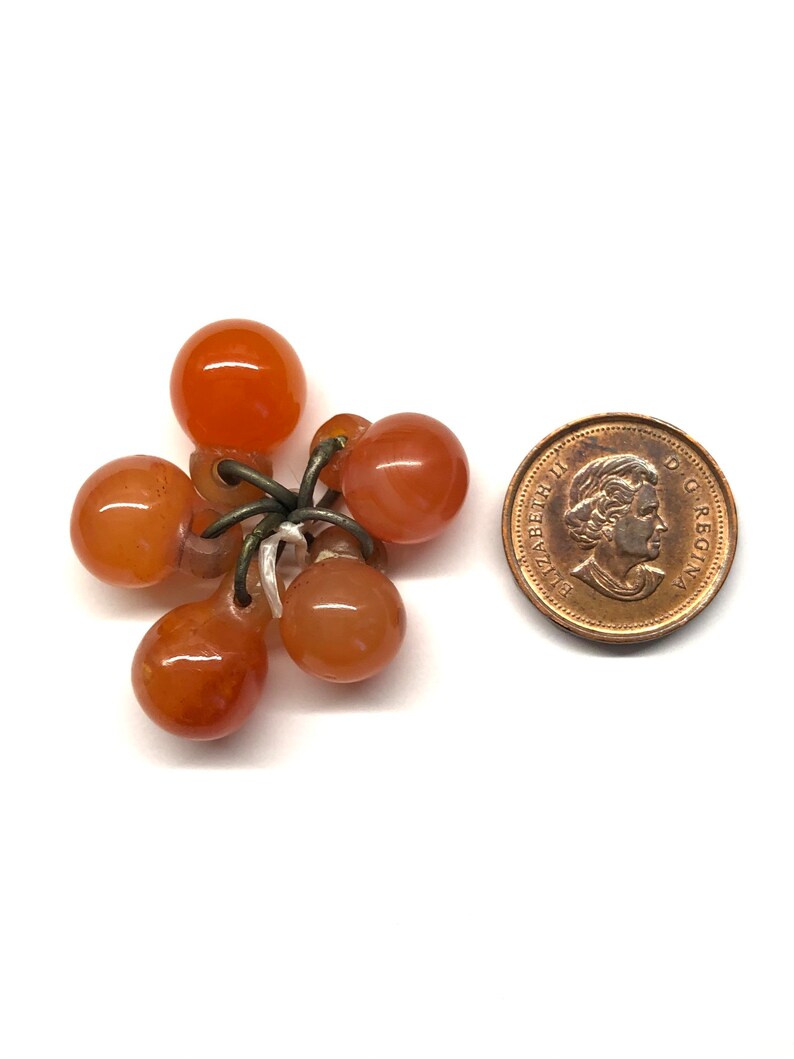 May include: A cluster of six small, orange-brown, round beads strung together with a silver wire. The beads are about the size of a dime.