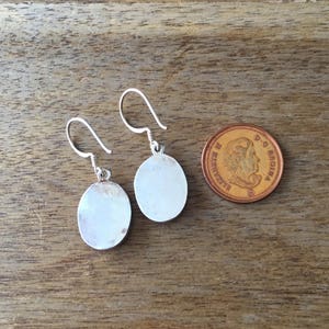 May include: A pair of silver earrings with round, smooth, silver discs. The earrings are approximately the size of a Canadian penny.