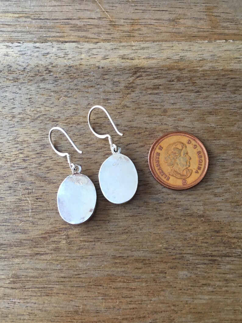 May include: A pair of silver earrings with round, smooth, silver discs. The earrings are approximately the size of a Canadian penny.