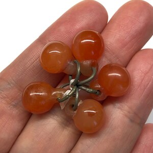 May include: A cluster of six carnelian beads connected by a silver wire. The beads are a deep orange color and have a smooth, polished finish.