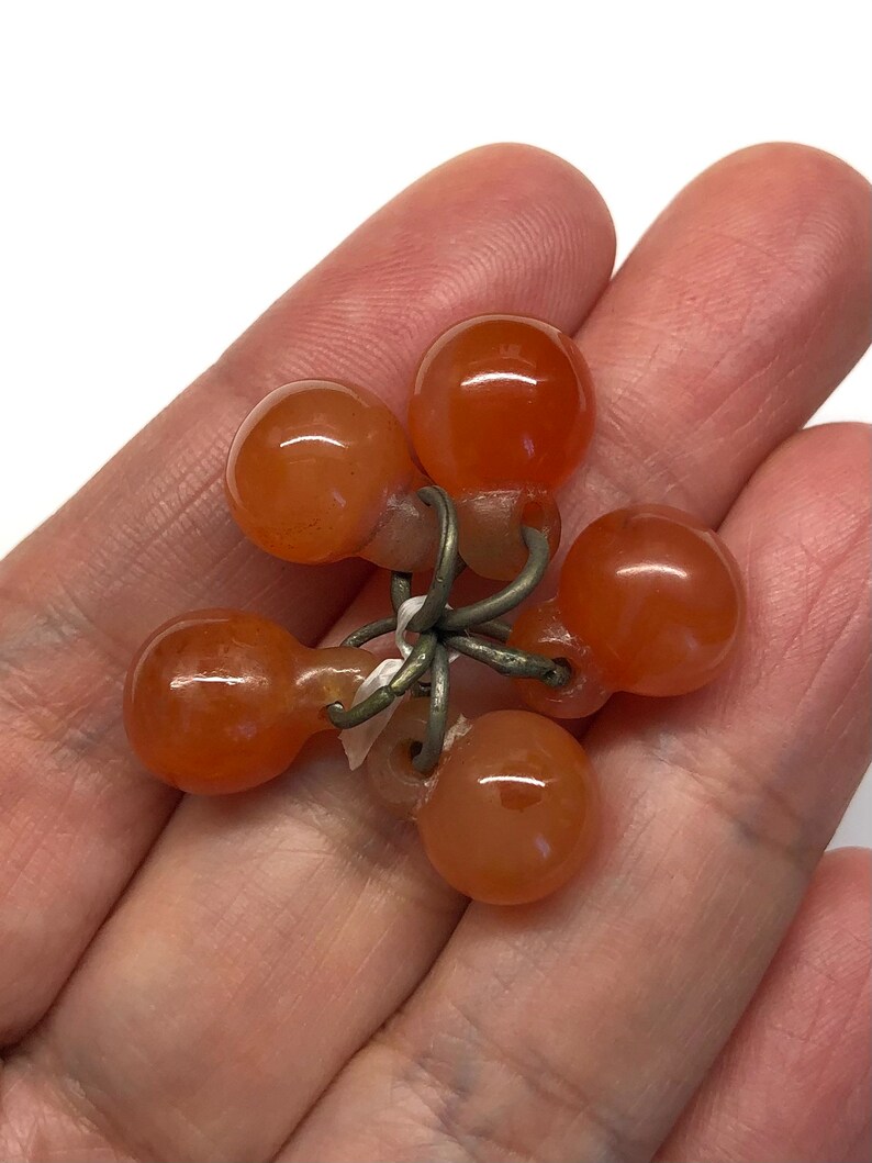 May include: A cluster of six carnelian beads connected by a silver wire. The beads are a deep orange color and have a smooth, polished finish.