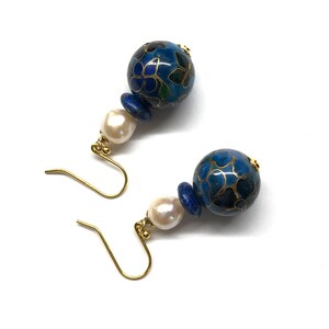 May include: A pair of blue and gold earrings with a white pearl accent. The earrings feature a round blue bead with a floral pattern and a smaller blue bead.
