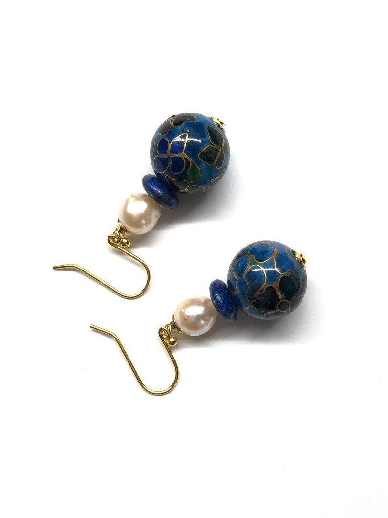May include: A pair of blue and gold earrings with a white pearl accent. The earrings feature a round blue bead with a floral pattern and a smaller blue bead.