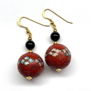 May include: A pair of red and black dangle earrings with gold hooks. The red beads are carved with floral designs and have white and blue accents.