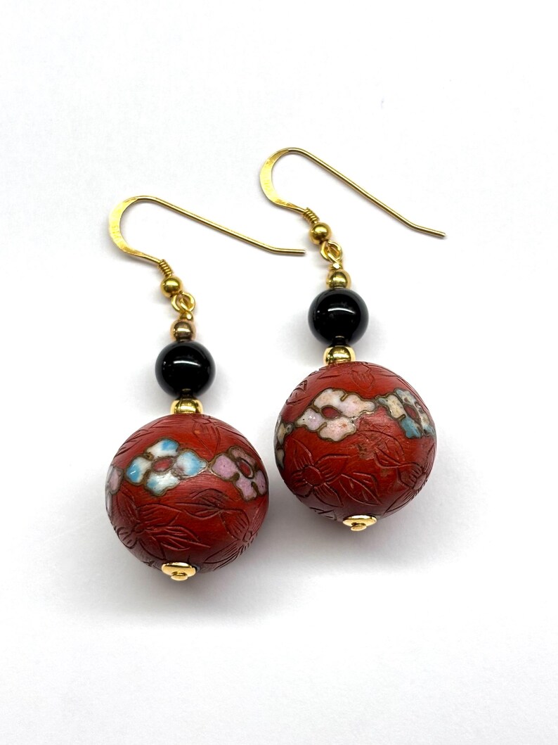 May include: A pair of red and black dangle earrings with gold hooks. The red beads are carved with floral designs and have white and blue accents.