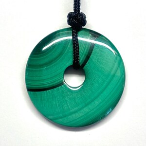 May include: A green malachite stone pendant in the shape of a donut, hanging from a black cord.