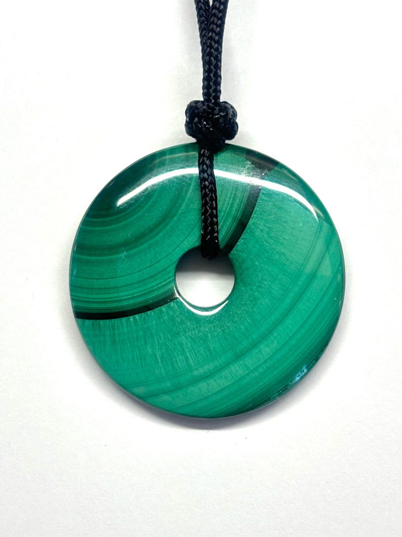 May include: A green malachite stone pendant in the shape of a donut, hanging from a black cord.