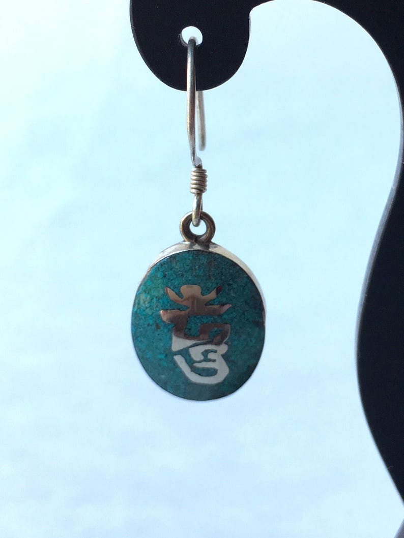 May include: Silver dangle earrings with a turquoise oval charm featuring a silver Chinese character.