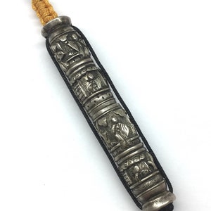 May include: A silver prayer wheel with intricate carvings and a black cord. The wheel is decorated with raised figures and designs.