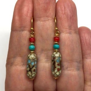 May include: Gold dangle earrings with a white, blue, and red patterned bead, turquoise bead, and coral bead.