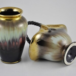 May include: Two ceramic vases with a brown, green and gold glaze. The vases have a unique, abstract design. One vase has a handle.