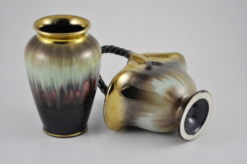 May include: Two ceramic vases with a brown, green and gold glaze. The vases have a unique, abstract design. One vase has a handle.
