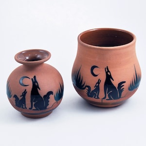 May include: Two terracotta pottery vases with black painted designs of howling wolves and a crescent moon. The smaller vase is on the left and the larger vase is on the right.
