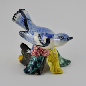 May include: A blue and white ceramic bird figurine perched on a branch with green and yellow leaves and red berries.