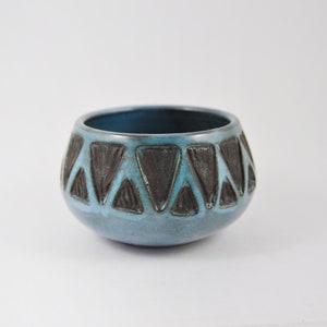 Peut inclure: Un petit bol en céramique bleu avec un motif géométrique de triangles noirs autour du bord.