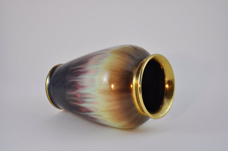 May include: A ceramic vase with a gold rim and a colourful, iridescent glaze. The glaze features shades of purple, brown, and green.