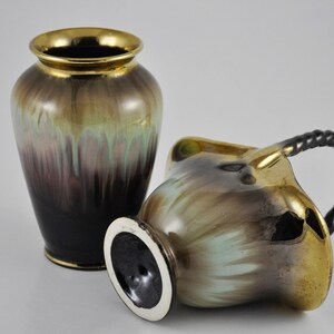 May include: Two ceramic vases with a gold, green and brown glaze. The larger vase is taller and has a rounder shape. The smaller vase has a handle and a more angular shape.