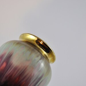 May include: A ceramic vase with an iridescent glaze in shades of purple, green, and brown. The vase has a gold rim around the top.