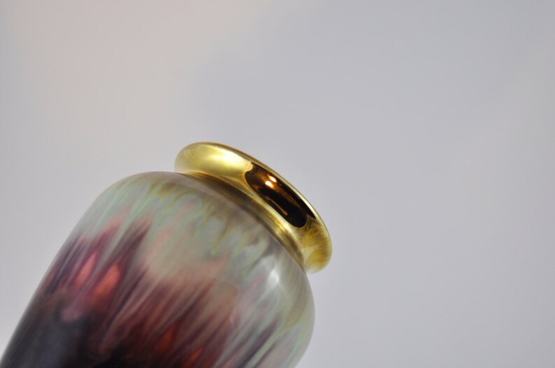 May include: A ceramic vase with an iridescent glaze in shades of purple, green, and brown. The vase has a gold rim around the top.