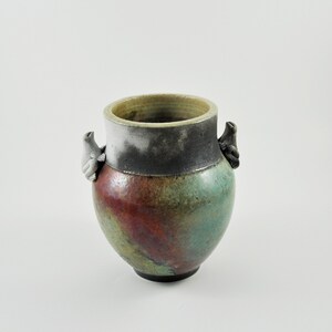 May include: A ceramic vase with a green, red and brown glaze. The vase has two small, sculpted bird handles on either side.