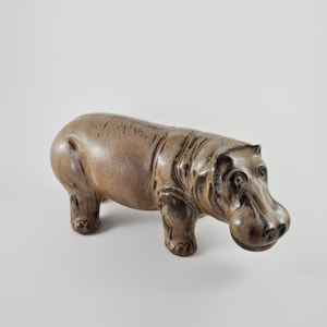May include: A ceramic hippopotamus figurine with a brown and black glaze. The hippo is standing on all fours with its head turned to the side.